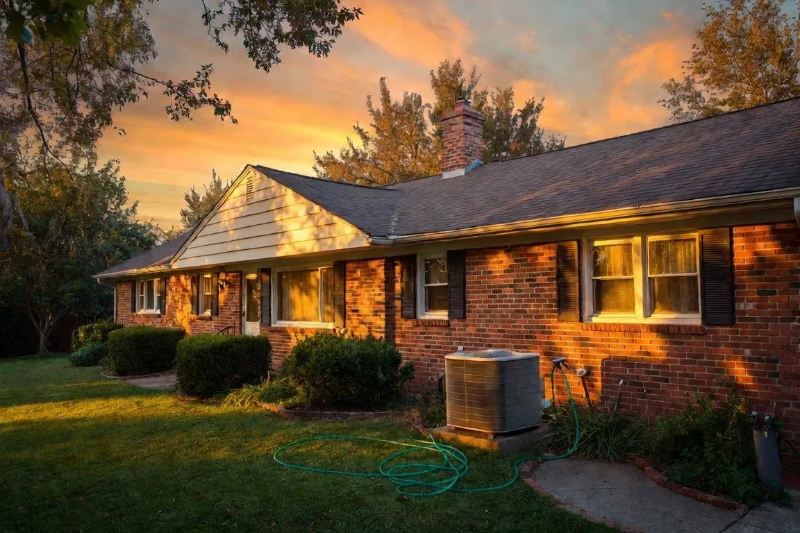 A well-kept 1970s brick ranch house at golden hour with an aging AC unit beside the wall